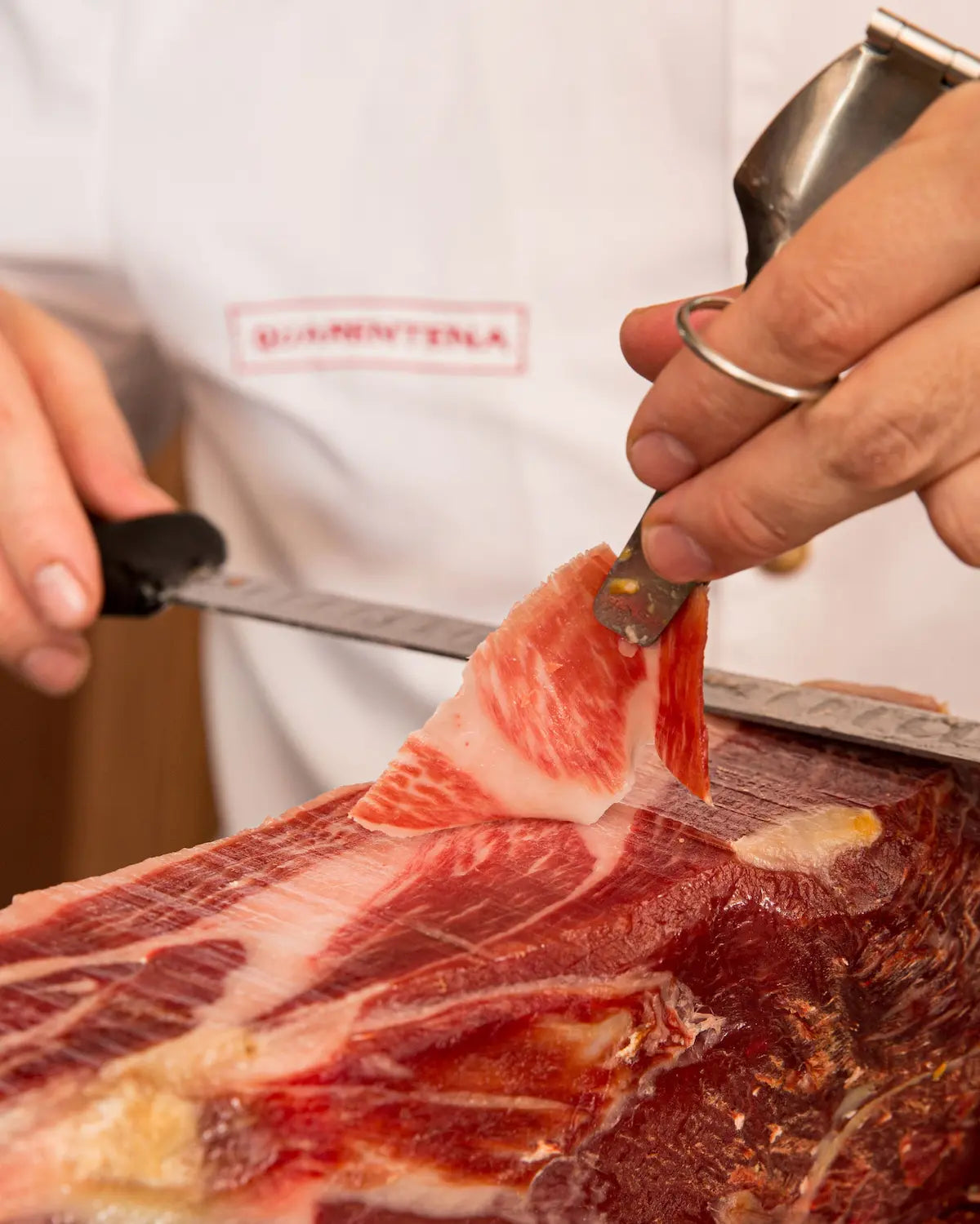 Person cutting a piece of meat with a knife, wearing a white apron with 'Almonte' branding.