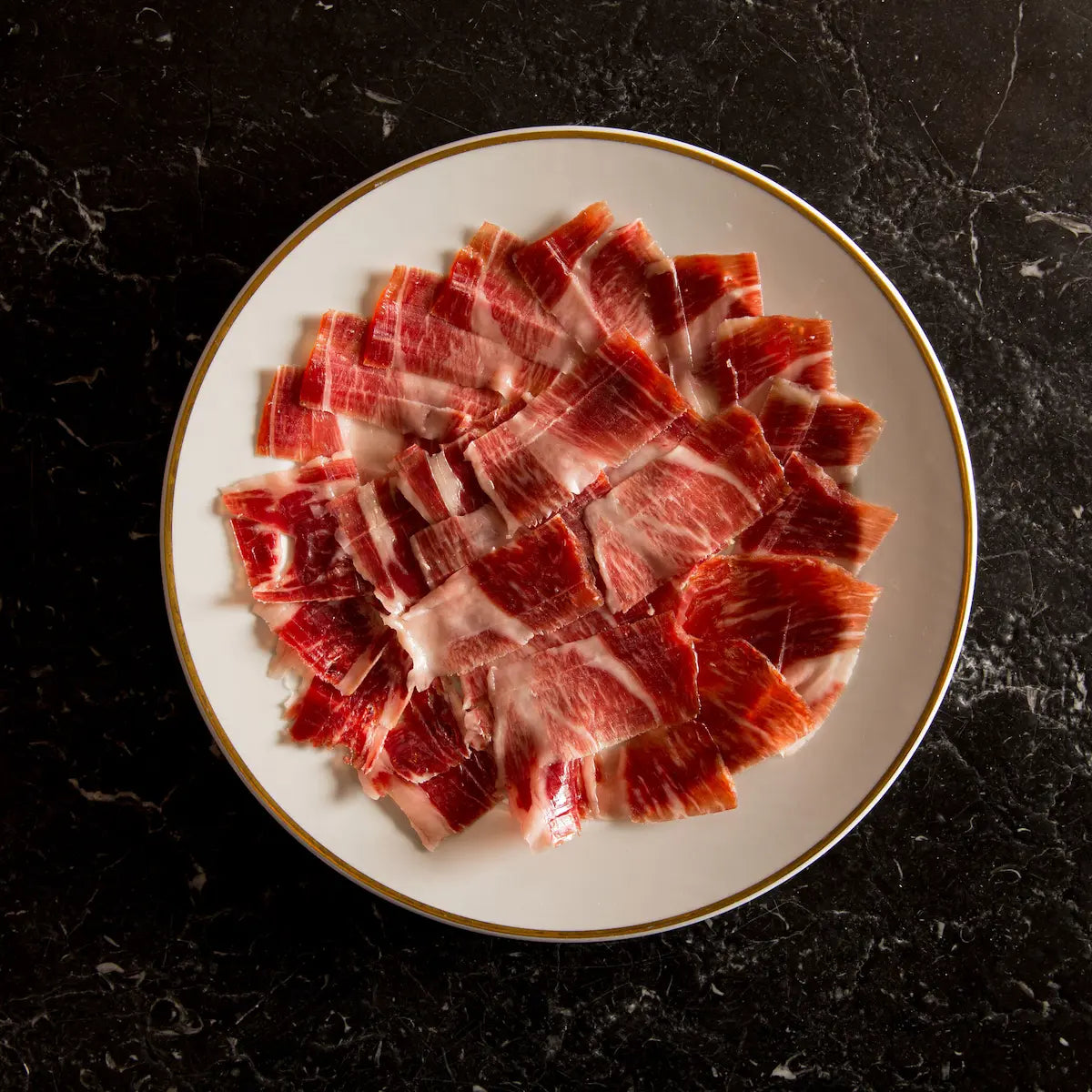 Sliced raw meat on a white plate with a gold rim against a dark background