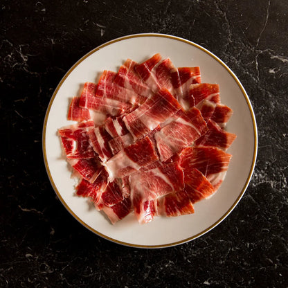 Sliced raw meat on a white plate with a gold rim against a dark background