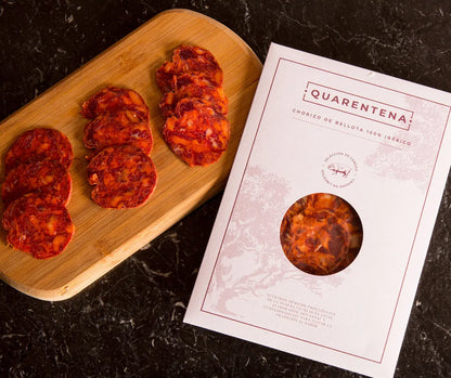 Wooden board with pepperoni slices and a 'Quarentena' product packaging on a dark surface.