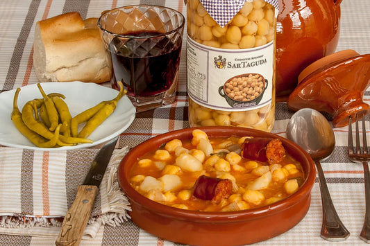 Bowl of chickpea stew with a jar of San Tagua chickpeas on a patterned tablecloth.